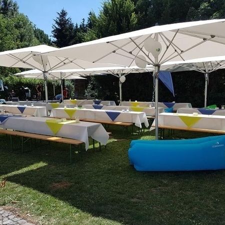 Gemütliche Tische und Stühle auf einer Wiese, geschützt durch große Sonnenschirme.