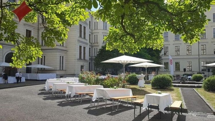 Ein Innenhof mit Tischen und Sonnenschirmen vor einem Gebäude.