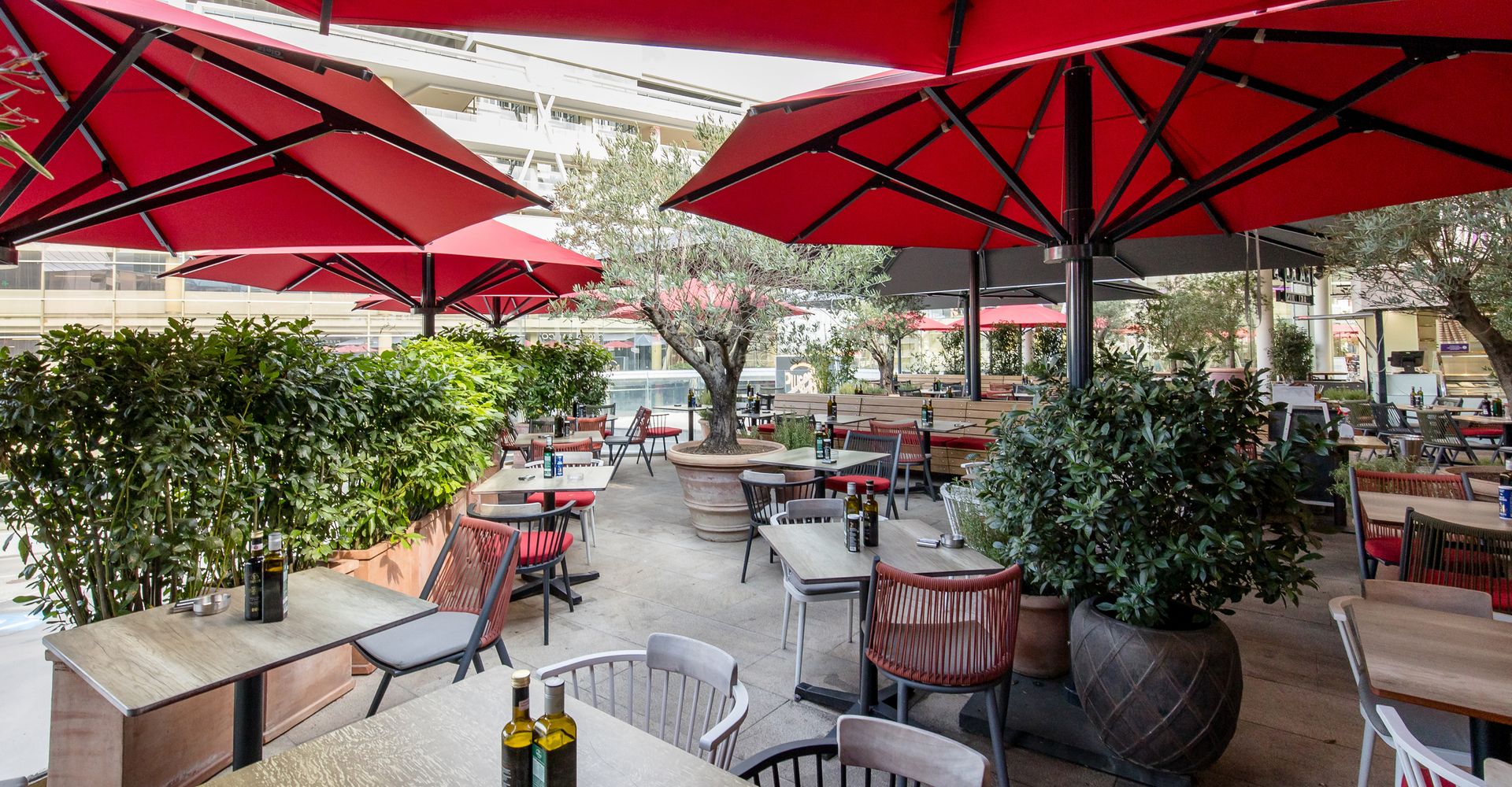 Gemütlicher Außenbereich eines Restaurants mit roten Sonnenschirmen und Pflanzen.