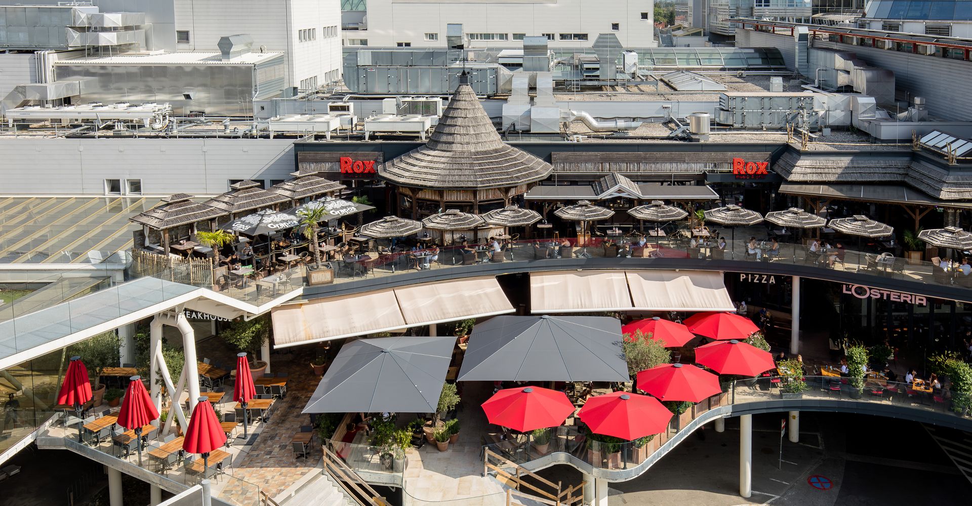 Terrasse eines Restaurants mit roten Sonnenschirmen und Sitzplätzen im Freien